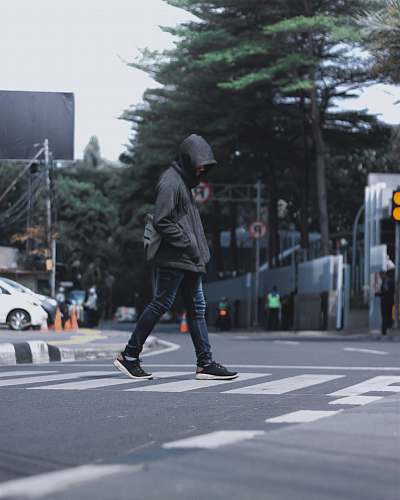 tarmac photography of man wearing black hooded jacket and blue denim jeans passing by the pedestrian lane road