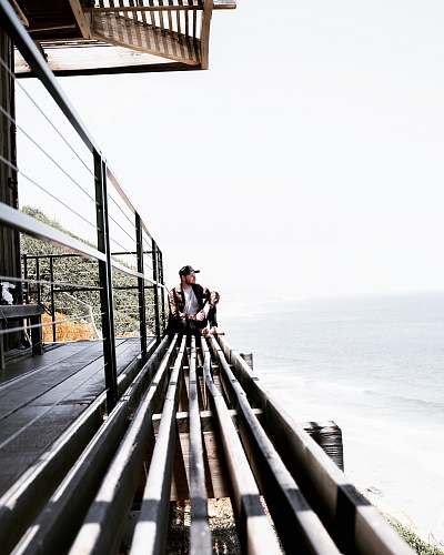 handrail man sitting on grey surface near ocean railing