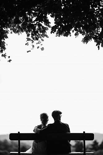 white couple sitting on bench under tree grayscale photography person