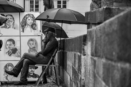 person grayscale man selling paintings on street umbrella