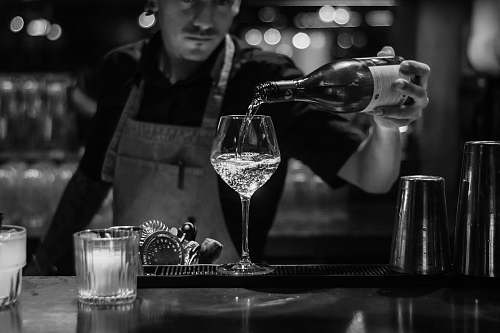 glass grayscale photo of bartender pouring liquid in wine glass human