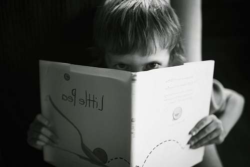 people grayscale photo of boy holding book reading