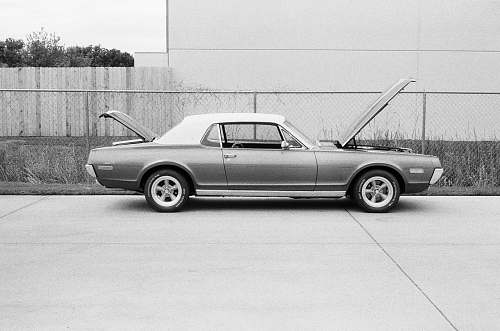 tire grayscale photo of coupe parked near fence machine