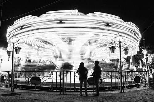 human grayscale photo of man and woman standing near carousel person