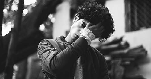 people grayscale photo of man in jacket putting his palm on his forehead human