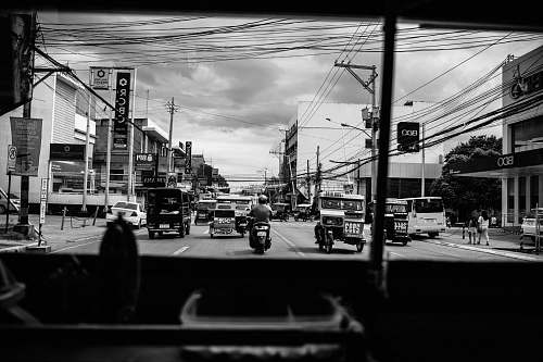 grey grayscale photo of man riding on motorcycle in road near buildings urban