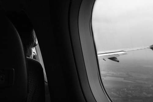 flight grayscale photo of man sitting near airliner window plane