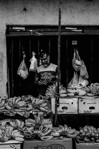 human grayscale photo of man standing beside banana fruits person