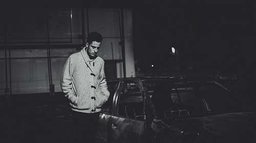 man grayscale photo of man standing beside car male
