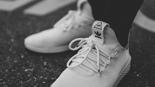 grey grayscale photo of person in white adidas low-top sneakers shoe