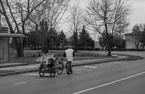 human grayscale photo of person walking beside trike person