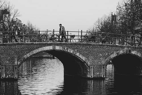building grayscale photo of person walking on bridge water