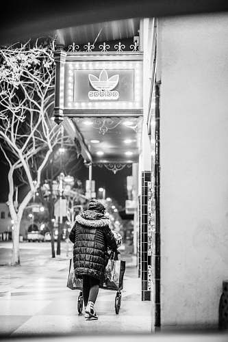 human grayscale photo of person walking on sidewalk near Adidas store people