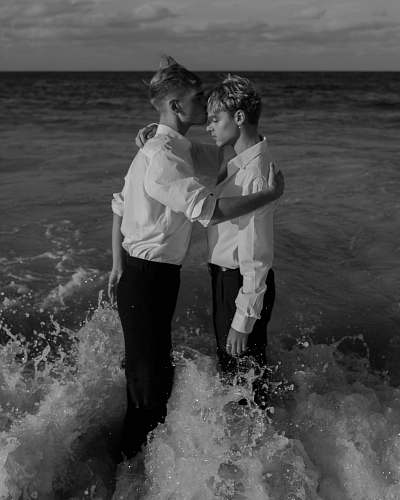 sea grayscale photo of two man standing on body of water water