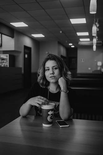 human grayscale photo of woman holding disposable cup with straw on table people