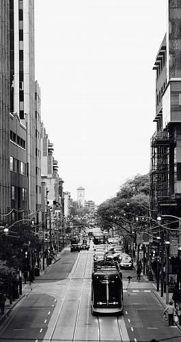 human grayscale photography of a tram passing by city street pedestrian
