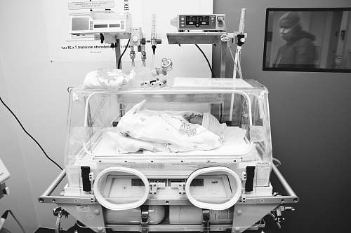 human grayscale photography of baby inside medical equipment person
