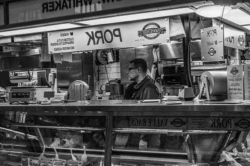 person grayscale photography of man inside pork food counter human