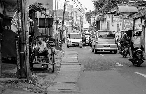 human grayscale photography of man sitting on chair near road street