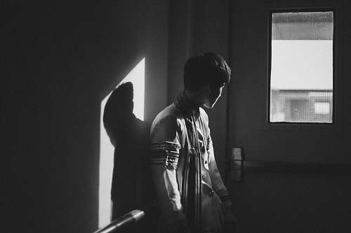 human grayscale photography of man standing beside door person
