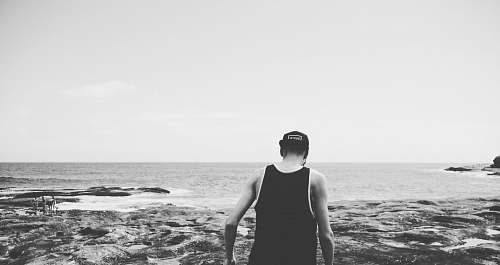 nature grayscale photography of man walking on shore outdoors