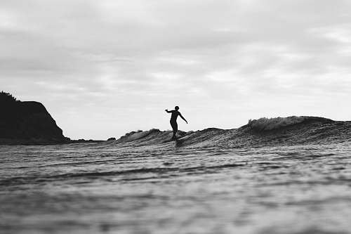 water grayscale photography of person surfing on sea ocean