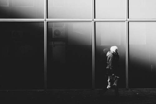 human grayscale photography of person walking near glass window building person