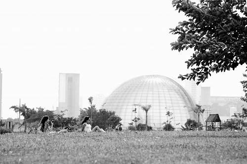 human grayscale photography of two women sitting on grass person