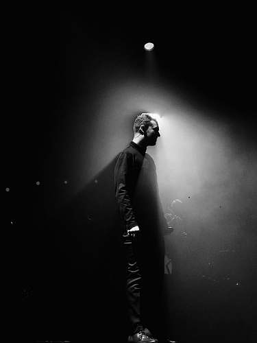 lighting grayscale photography of unknown person standing spotlight