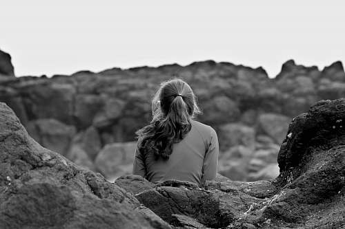 blonde grayscale photography of woman sitting on rock woman