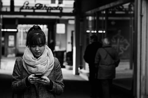 apparel grayscale photography of woman walking near street while using smartphone clothing