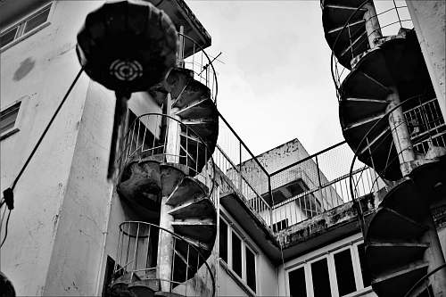 banister grey scale photography of spiral stairs beside building handrail