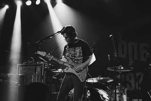 person greyscale photo of man playing electric guitar on stage guitar
