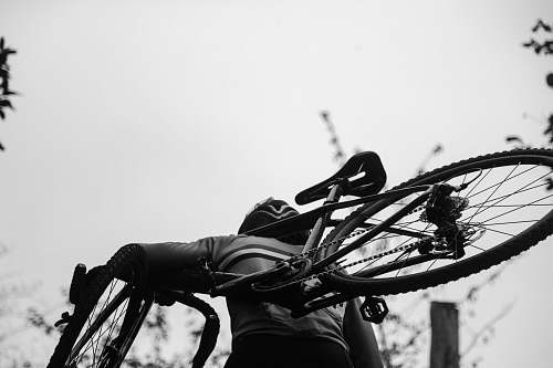 bike greyscale photography of man carrying bike bicycle