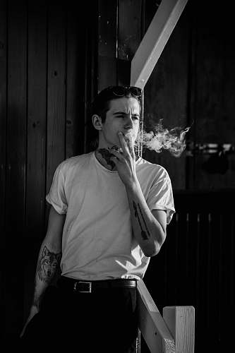 human man leaning on wooden handrail while smoking skin
