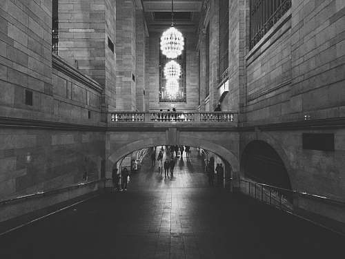 architecture people walking on hallway of concrete building with turned on chandelier lights in grayscale photography new york