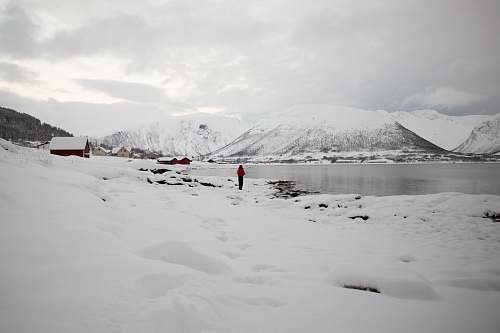 grey person standing beside lake near covered snow mountain during daytime mountain