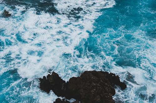 water aerial photography of black rock formations near seawaves ocean