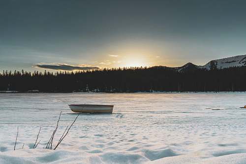 rowboat boat on frozen lake with silhouette of trees at distance transportation