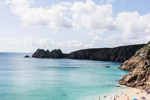 promontory body of water across mountain during white cloudy sky beach