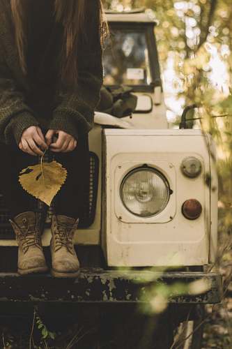 plant woman in gray sweater holding withered leaf while sitting on white vehicle jar