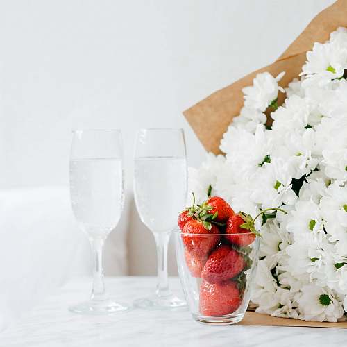 strawberry red strawberries filled glass cup beside white flower bouquet bedside