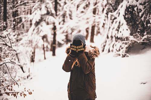 human person standing on snow field surrounded by trees covering his face with his hands tree