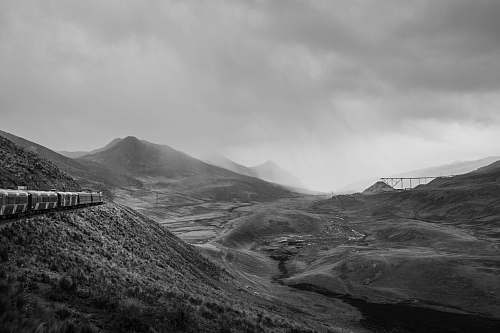 nature grayscale photo of train beside of mountain during cloudy sky black-and-white