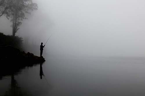 fishing man fishing on calm water behind tree fog