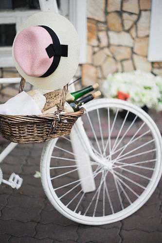 bicycle brown wicker basket with white, pink, and black sunhat besides white bike bike