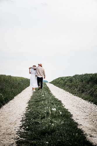 apparel man and woman walking on pathway beside green bush clothing