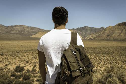person man standing in front dried grass field near gray mountains under gray sky people
