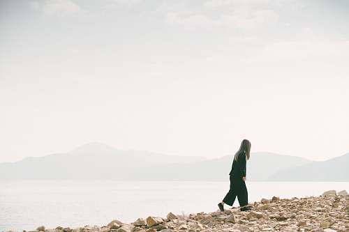 person man walking on brown concrete rocks under gray sky people