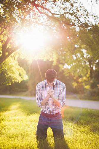 people photo of man kneeling on grass near tree light